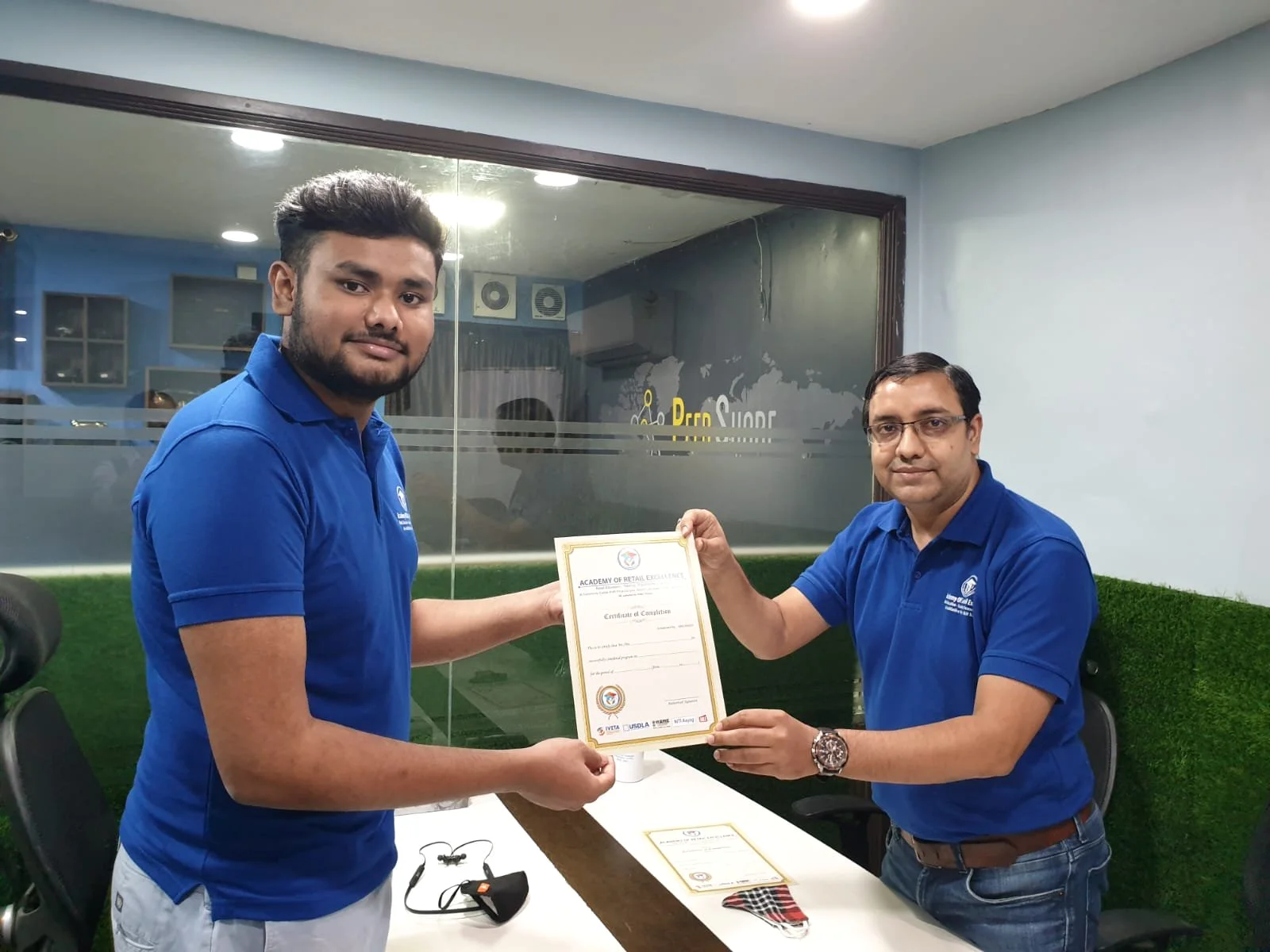 An Academy of Retail Excellence certificate being handed to a student. Sign visible in the photograph: Certificate of Completion.