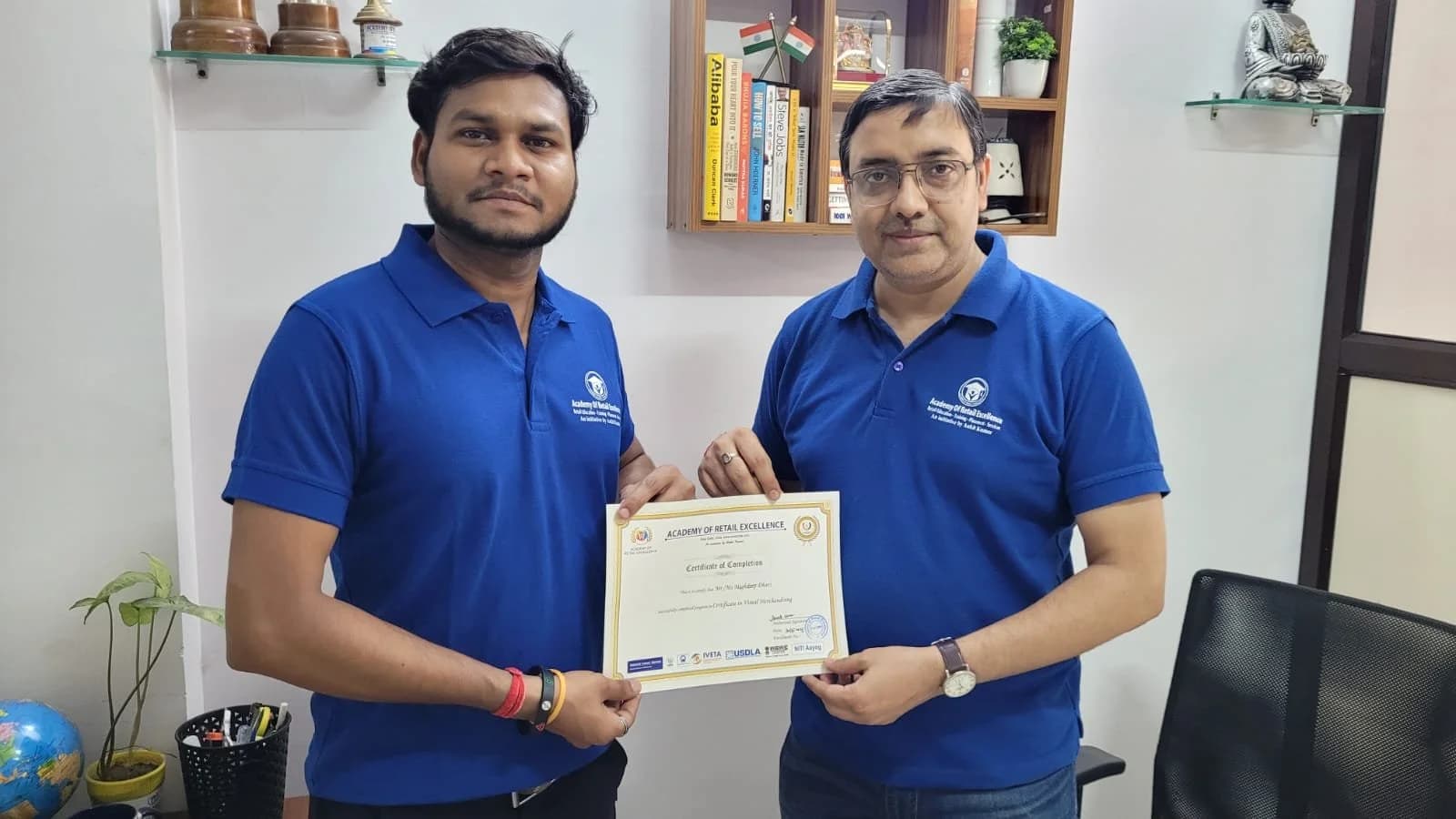 An Academy of Retail Excellence certificate being handed to a student. Sign visible in the photograph: Certificate in Visual Merchandising.